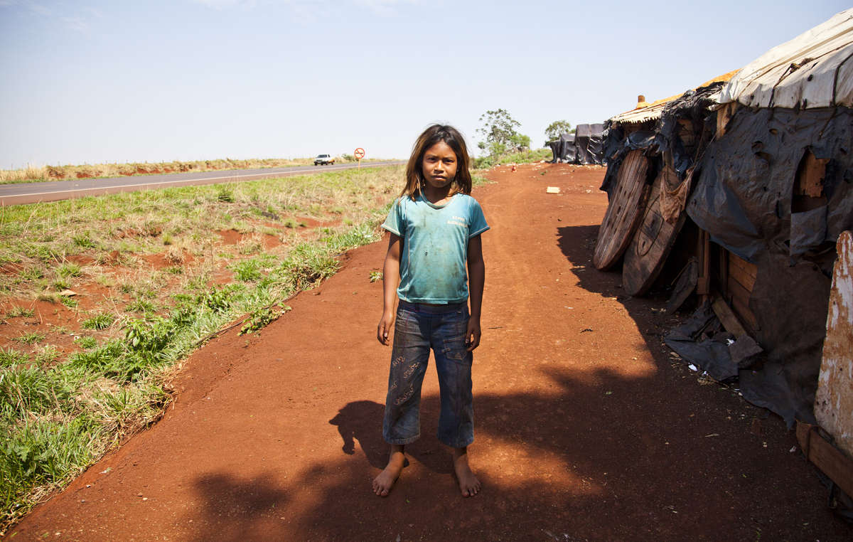 Fillette guarani devant son abri en bord de route - des champs sans fin ont remplacé la forêt luxuriante de son peuple. Beaucoup d'enfants se sont suicidé, la plus jeune n'avait que neuf ans.