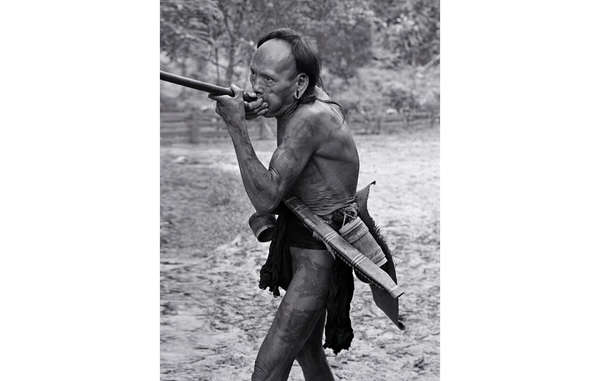 A nomadic Penan hunter-gatherer in Sarawak, Malaysia, using a blowpipe (1976). His loincloth is made from a long strip of soft, beaten bark, and around his waist is everything he needs in the forest: a sharp parang in its wooden sheath and a small container to hold spare poison darts.