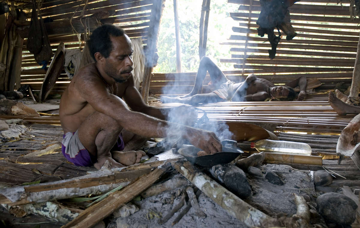 Ein Korowai backt Sago über dem Feuer, West-Papua.