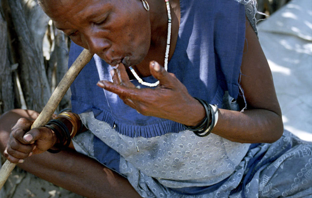 Uma mulher Bosquímana mastiga um pedaço de melão por sua água, na comunidade Metsiamenong, Botsuana. Os melões são cultivados pelos Bosquímanos e são uma fonte de água importante.