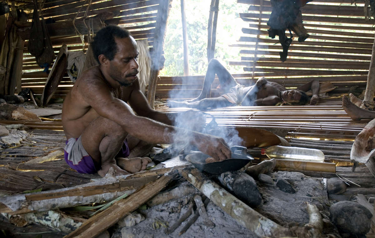 Un hombre korowai cocina sago en el fuego, Papúa Occidental.