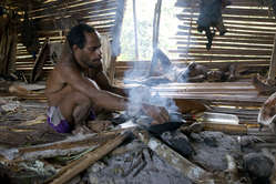 Un hombre korowai cocina sago en el fuego, Papúa Occidental.