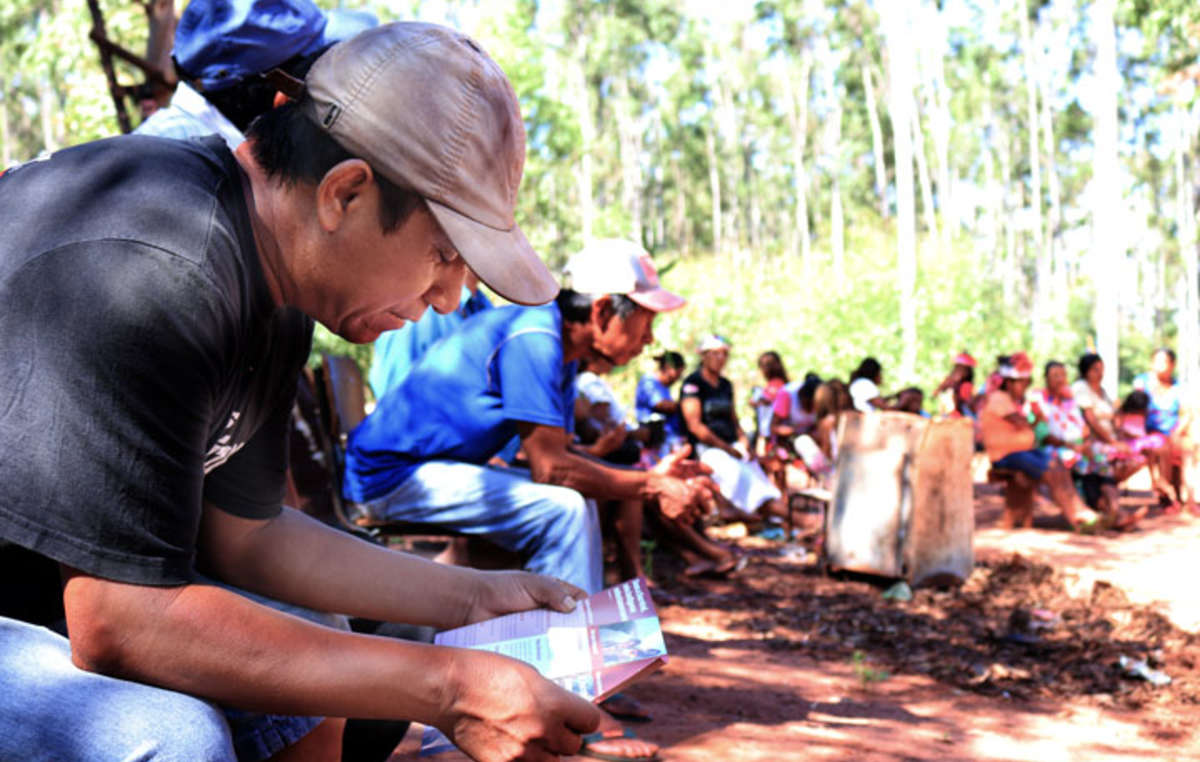 Bei einem Treffen der Gemeinde liest ein Guarani-Mann einen Flyer von Survival International, der globalen Bewegung für indigene Völker. Survival arbeitet seit den 70er-Jahren für die Guarani.