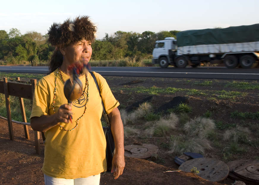 Damiana Cavanha se tient au bord d'une route brésilienne, une maraca ornée de plumes bleues dans une main, et commence à chanter. Le sol est jonché d'ordures; derrière elle se trouve sa maison construite dans un mélange de tôle ondulée, de plastique et de bâches.

Des camions passent à toute vitesse; le vacarme couvre ses invocations.
