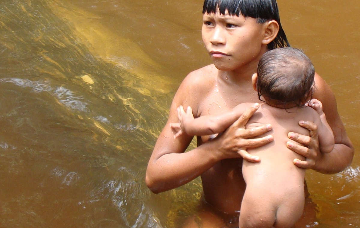 Un niño suruwaha baña a un bebé en un río.
