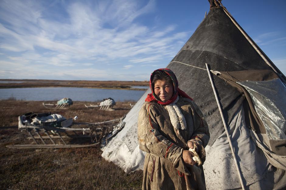 Eine Nenzin außerhalb ihres chum (Tipi) auf Sibiriens Jamal-Halbinsel. Ihre Heimat ist ein abgelegener, stürmischer Ort mitten im Permafrost, mit verschlungenen Flüssen und winzigen Sträuchern. Seit über tausend Jahren ziehen die Nenzen, nomadische Rentierhirten, durch das Gebiet.

Im Winter ertragen die Frauen Temperaturen, die bis zu -50 Grad erreichen. Dann lassen die meisten Nenzen ihre Rentiere an Moos und Flechten in den südlichen Wäldern oder der Taiga grasen. In den Sommermonaten, wenn die Mitternachtssonne die Nacht zum Tag macht, packen die Frauen das Lager zusammen und ziehen mit ihren Familien Richtung Norden.

Heute ist ihre Lebensweise durch Ölbohrungen und den Klimawandel beeinträchtigt. Die Infrastruktur, die mit der Ausbeutung der Rohstoffe in die Region kommt, geht auch an den Routen der Nenzen nicht spurlos vorbei: Straßen sind für die Rentiere schwer zu überqueren und die Nenzen sagen, dass die Verschmutzung die Qualität des Weidelandes bedroht.

„Das Rentier ist unsere Heimat, unser Essen, unsere Wärme und unser Transportmittel“, erklärt eine Nenzin.