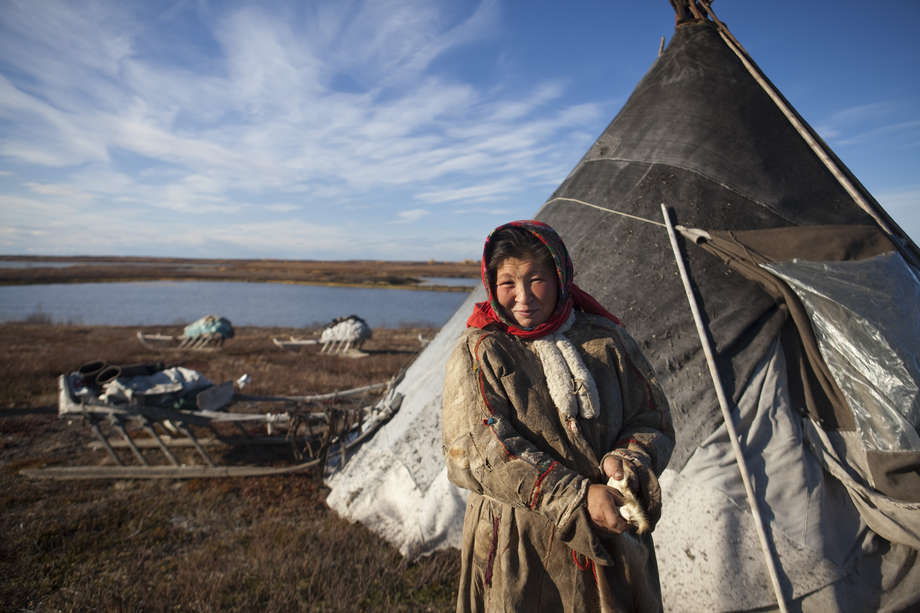 Une femme nenets devant son _chum_ (tipi) dans la péninsule de Yamal en Sibérie. Le territoire que les Nenets occupent depuis plus d'un millénaire est une étendue reculée, battue par les vents, au pergélisol entrecoupé de rivières sinueuses et de petits arbustes.

Durant l'hiver, la température peut descendre jusqu'à -50°. Les Nenets font alors paître leurs rennes sur les pâturages de mousse et de lichen des forêts du sud, ou taïga. Durant les mois d'été, lorsque le soleil de minuit transforme la nuit en jour, les femmes rangent leur campement et migrent vers le nord avec leur famille.

Aujourd'hui, leur mode de vie est gravement affecté par l'exploitation pétrolière et le changement climatique. Leurs routes migratoires sont perturbées par les infrastructures liées à l'extraction des ressources; les routes représentent des obstacles difficiles à franchir pour les rennes et la pollution menace la qualité des pâturages.

_Le renne est notre maison, notre nourriture, notre chaleur et notre moyen de transport_, rapporte une femme nenets.