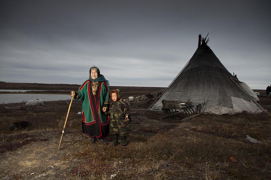 Far above the Arctic Circle, a Nenets reindeer herding woman and child stand outside their _chum_ (tipi)  on the Yamal Peninsula, a stretch of peatland that extends from northern Siberia into the Kara Sea.

Nenets women traditionally gave birth in their _chums_, and made diapers from cloth filled with moss. Today, they more commonly give birth in hospitals, having been collected by helicopter.