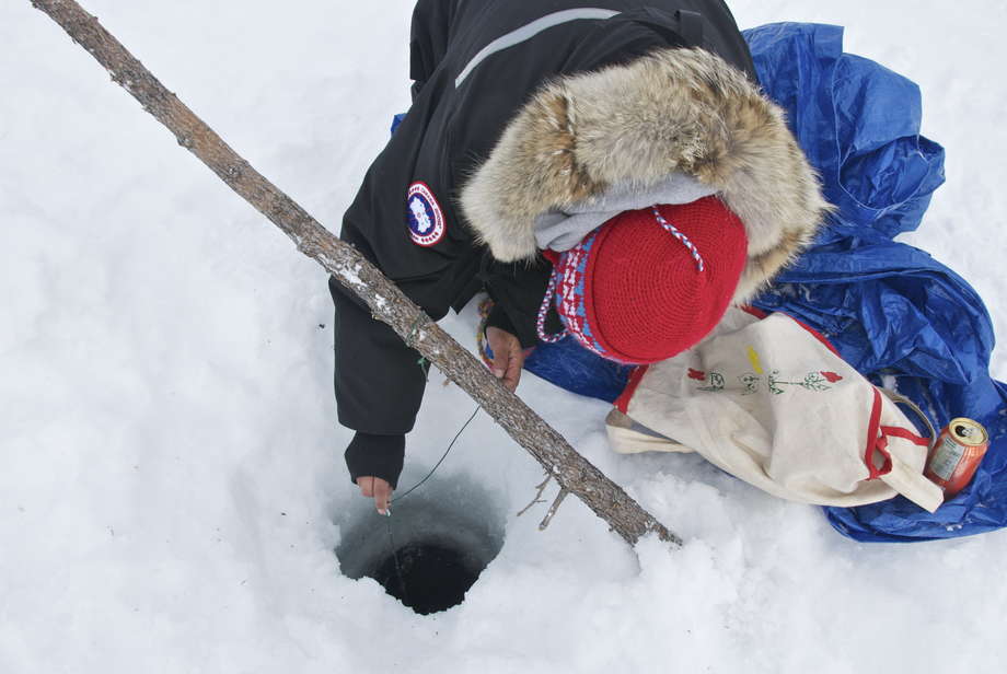 Innu-Frauen haben tiefe Löcher in das Eis gebohrt, um nach Seeforellen zu fischen.


