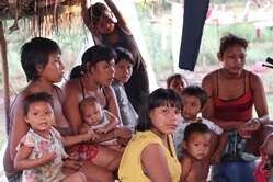 Mujeres y niños nukak se reúnen alrededor de un teléfono para ver dibujos animados por la noche en un reasentamiento nukak en la Amazonía colombiana