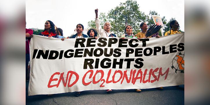 Photo of Indigenous activists holding a big canvas that reads: Respect Indigenous Peoples rights. End Co2lonialism