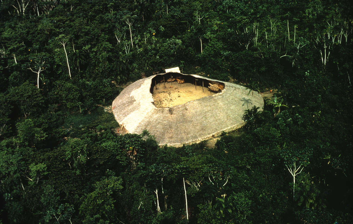 Eine Yanomami-Maloca. Die Yanomami leben in großen runden Gemeinschaftshäusern namens Yanos oder Shabonos. Einige können bis zu 400 Personen aufnehmen. Der zentrale Bereich wird für Aktivitäten wie Rituale, Feste und Spiele genutzt.