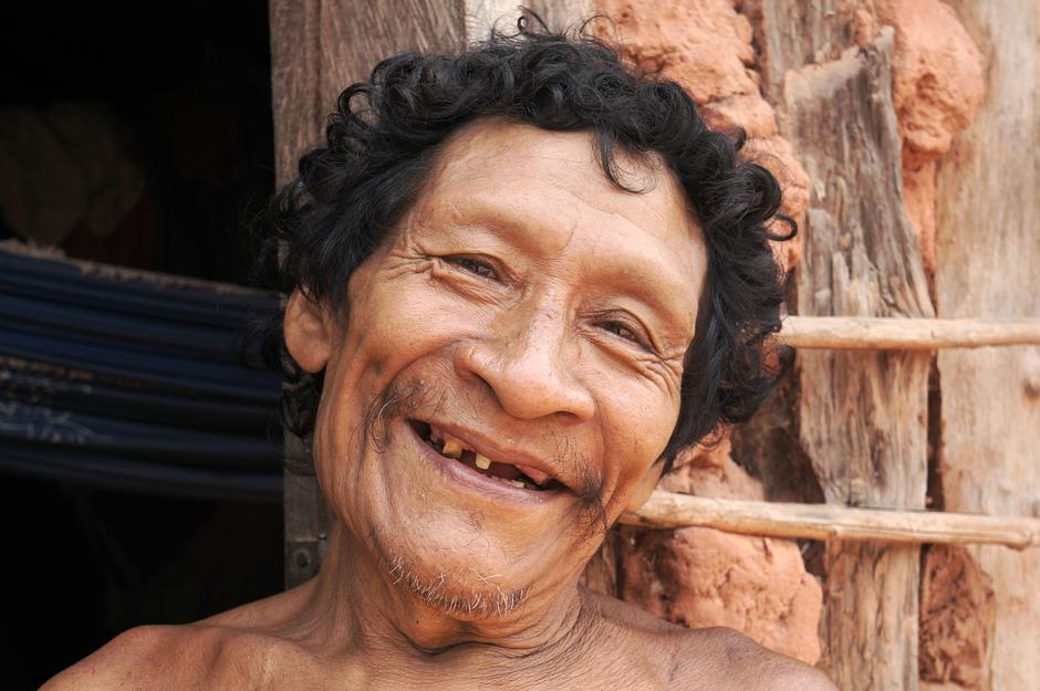 Karapiru, an Awá father, smiles at the camera at his home in Maranhão state, Brazil.  

His expression belies the trauma he has endured at the hands of invaders to his ancestral lands. After witnessing the massacre of most of his family by _karai_, or 'non-Indians', Karapiru fled into the rainforest where he remained on the run, in solitude, for ten long years. 

When he finally emerged from the rainforest, government officials sent a young man to talk to him. One word instantly transformed Karapiru's life: the young man said, _Father!_, for the young translator was Karapiru's son, who had miraculously survived the brutal attack.

Karapiru has now returned to an Awá village, but his tribe's problems are far from over. Their forests are disappearing faster than in any other indigenous area in the Brazilian Amazon.
