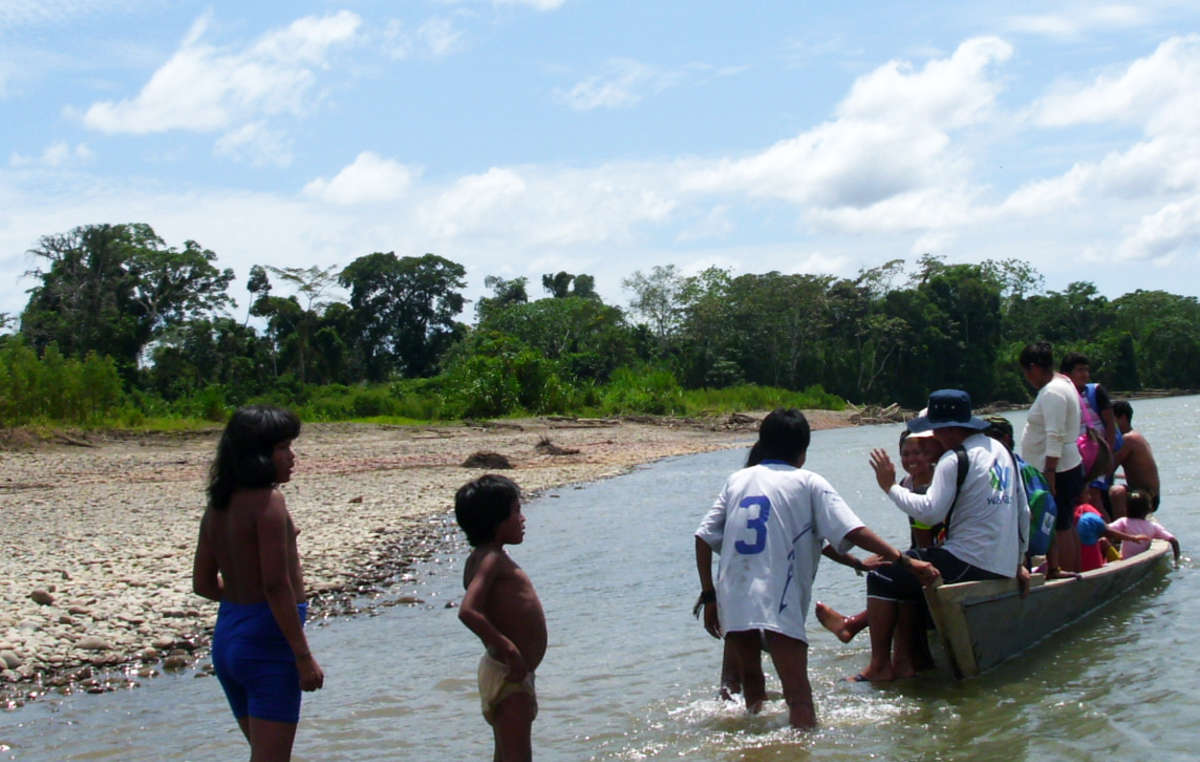 Une embarcation transportant des riverains locaux accoste sur la berge à proximité des Mashco-Piro dont les enfants portent des vêtements qu'ils viennent de recevoir.